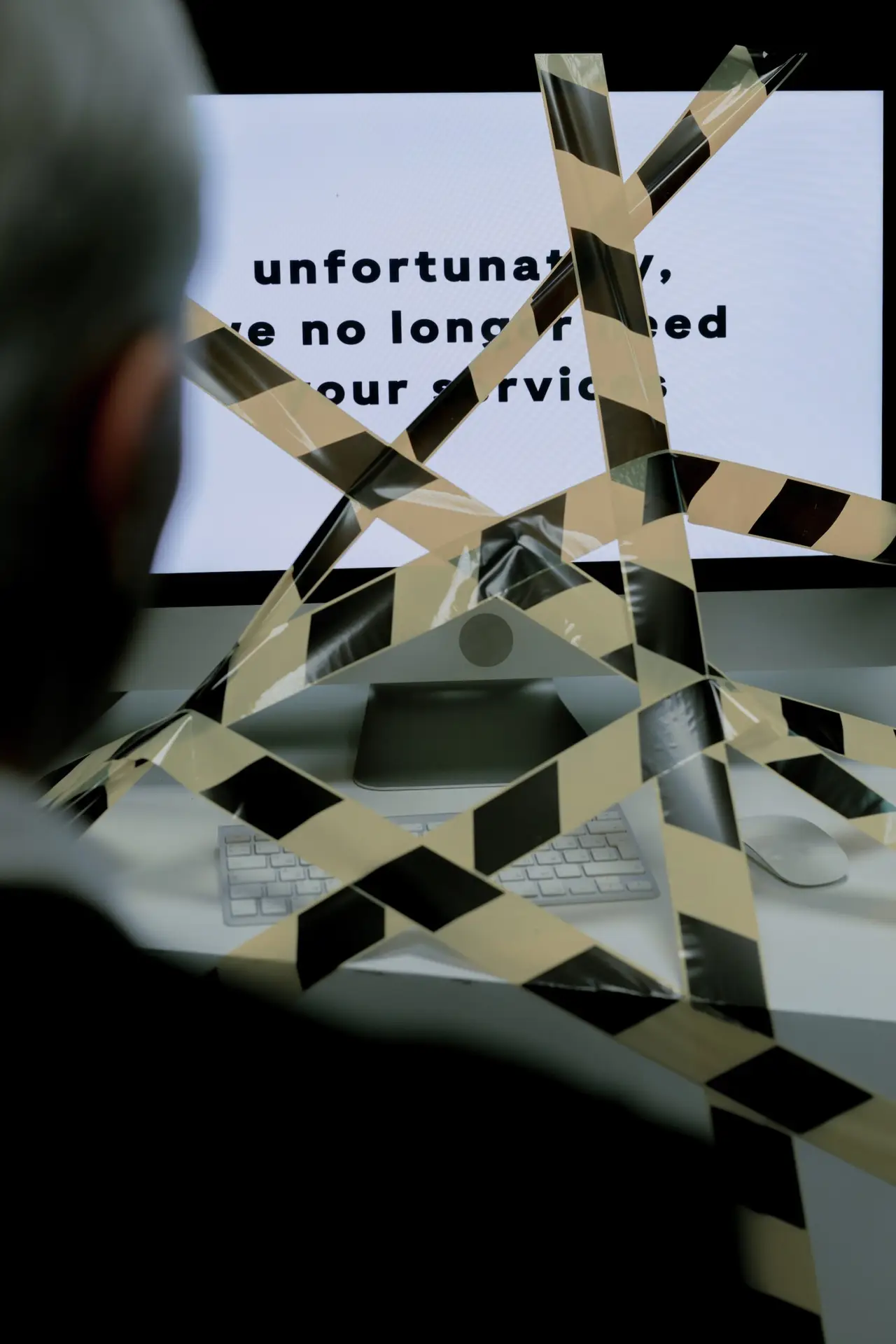 Unfortunately We No Longer Need Your Services computer screensaver with guy looking at computer wrapped in caution tape