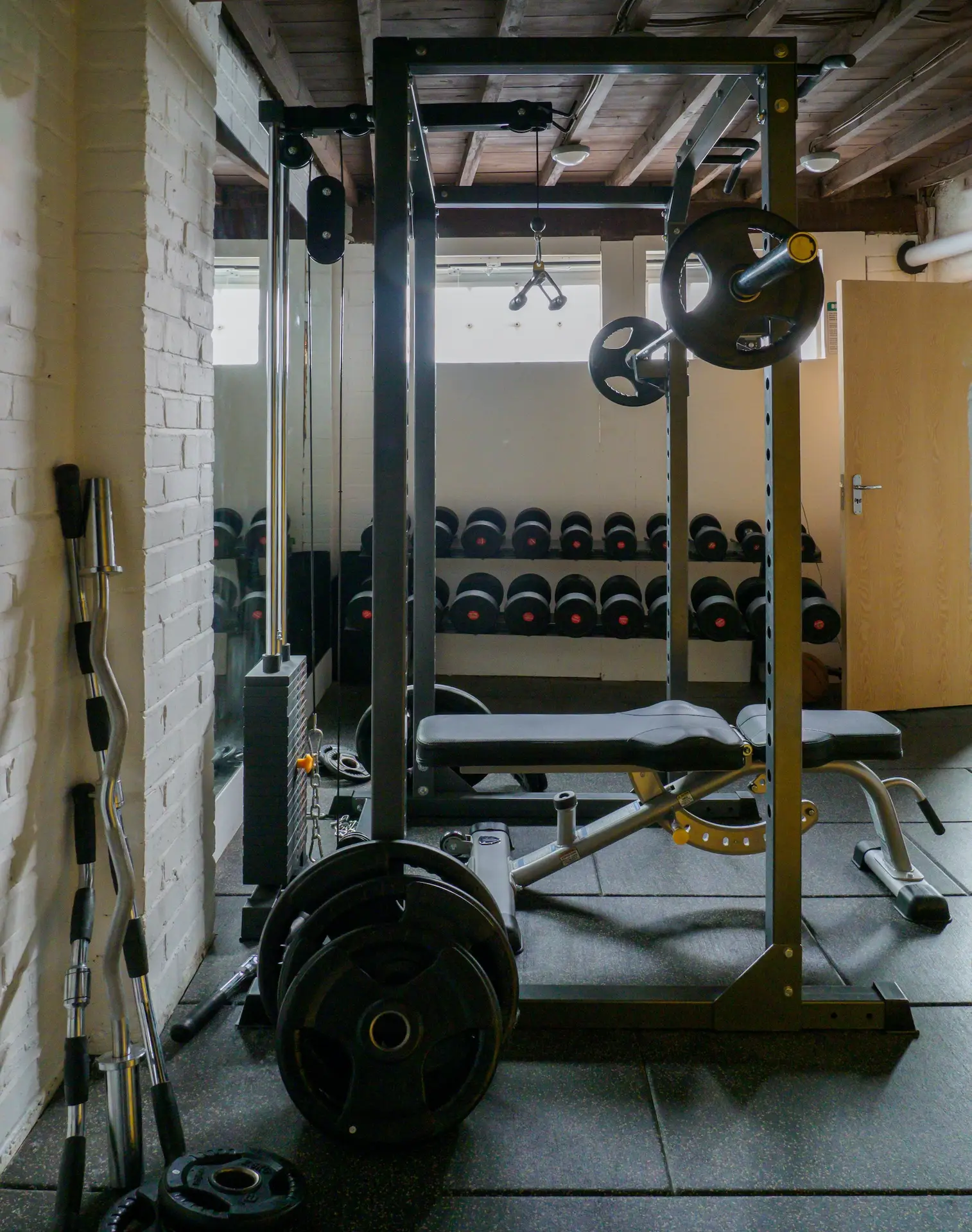 Best Home Gym Set Up Squat Rack with bench, dumbells, curl bar in the wall, and mirror behind bench